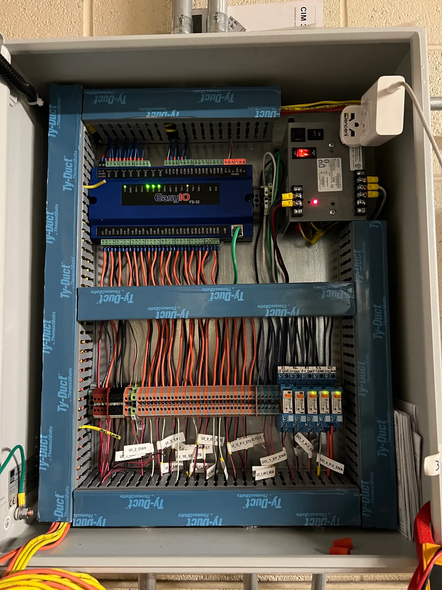Installed building automation control panel with DDC controller, labeled control wiring, and DIN-rail terminals